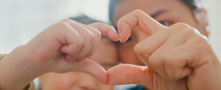 Mother and adopted daughter forming a heart shape with fingers